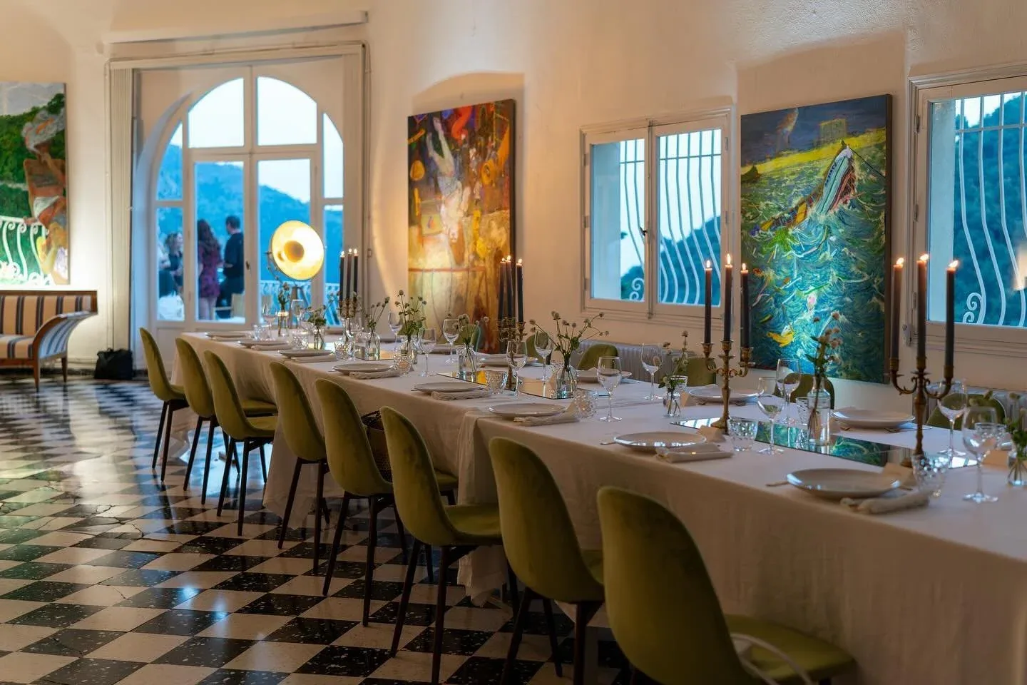 A long dinner table set in the salon at Castel Caramel, with paintings on the walls